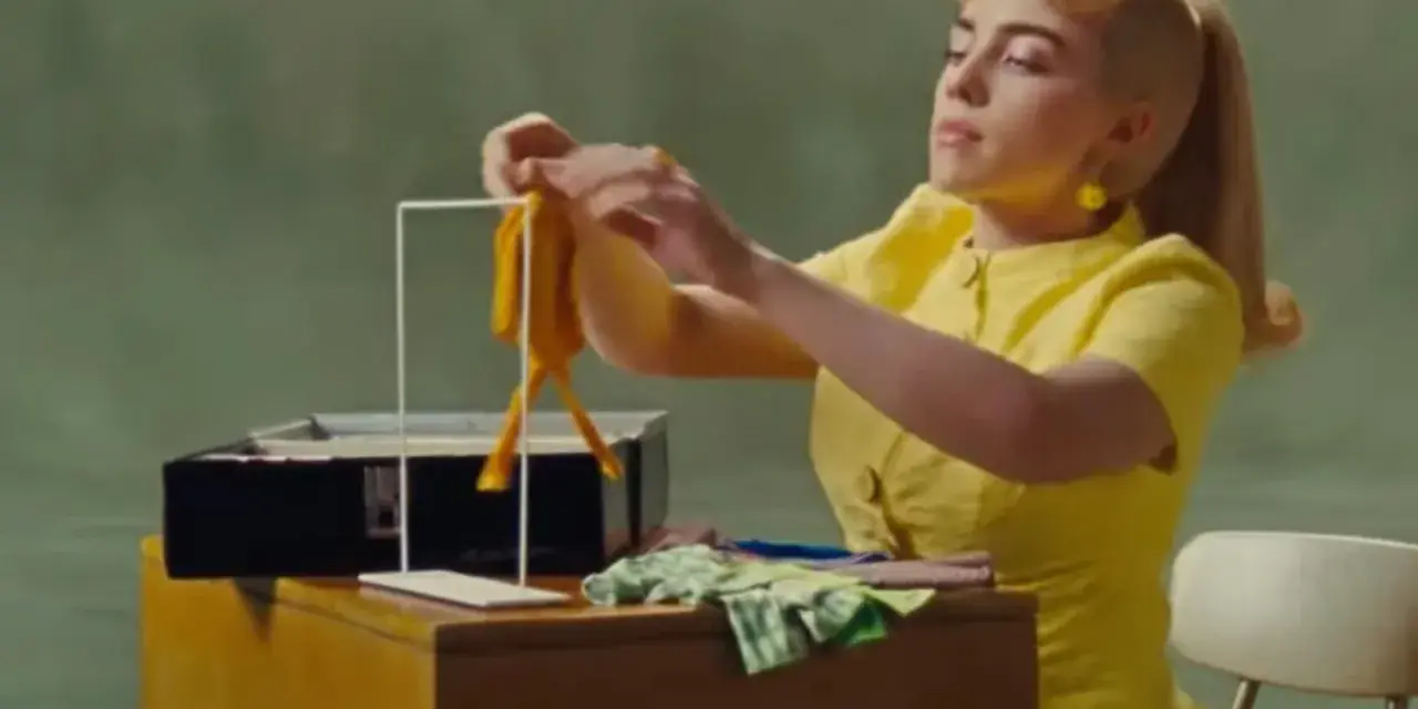 Billie Eilish w żółtej sukience, tworząca coś, co przypomina lalkę, w klimacie "What Was I Made For".