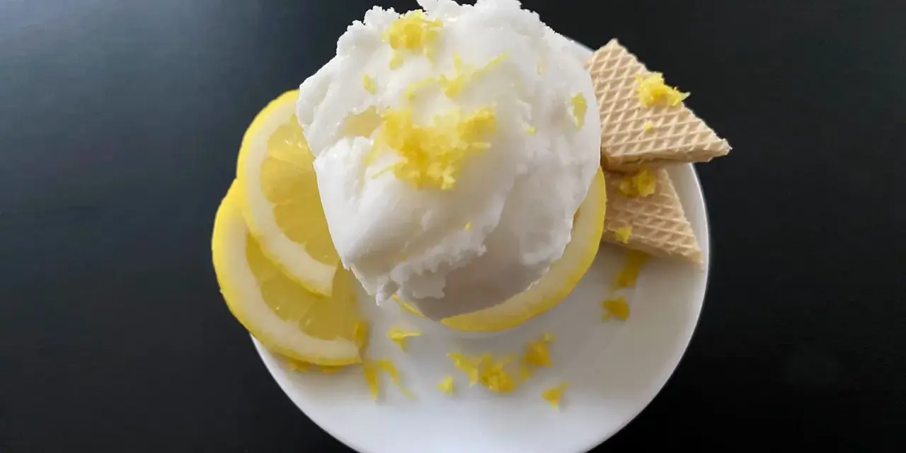 Erfrischendes zitroneneis wie beim Italiener, garniert mit Zitronenschale, Zitronenscheiben und Waffeln auf einem weißen Teller.