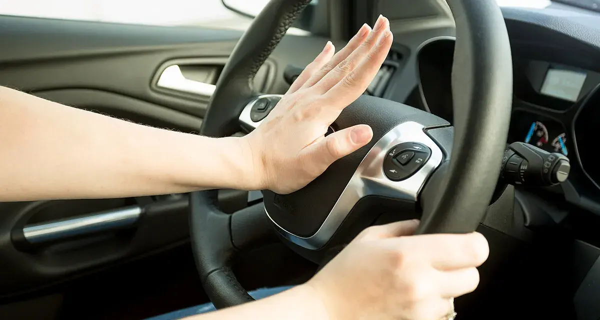 Hand drückt auf Hupe im Auto. Wann darf man hupen? Nur in Notfällen, um einen Unfall zu vermeiden.