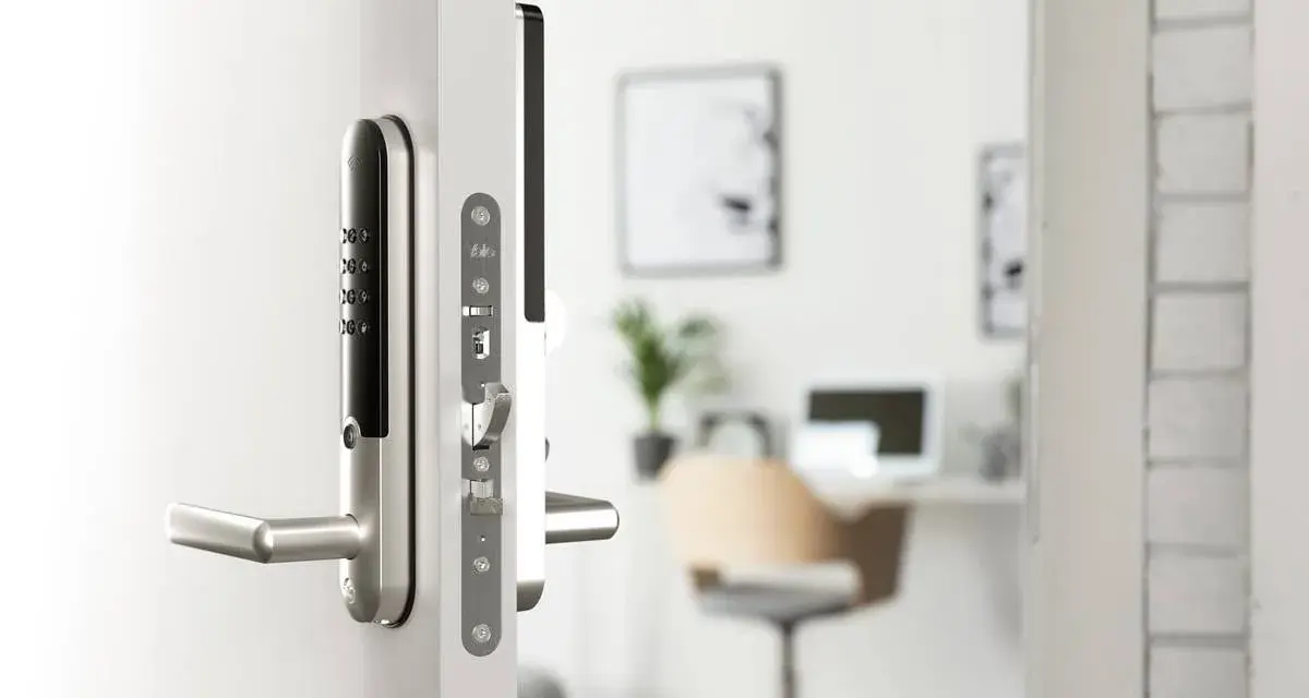 Modernt digitalt låssystem på en vit dörr. I bakgrunden syns ett kontor med skrivbord och stol.