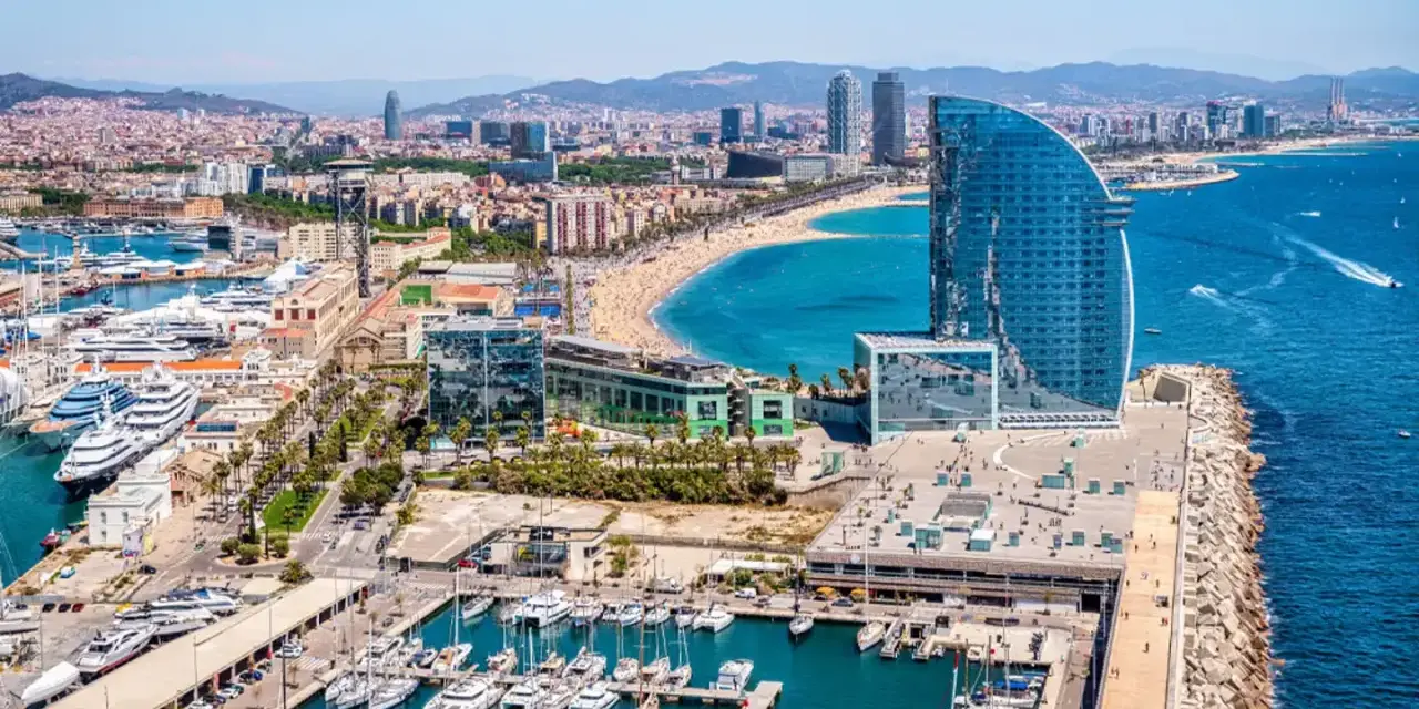 Barcelona morze: luksusowe jachty w marinie, plaża pełna ludzi i nowoczesny hotel w kształcie żagla.
