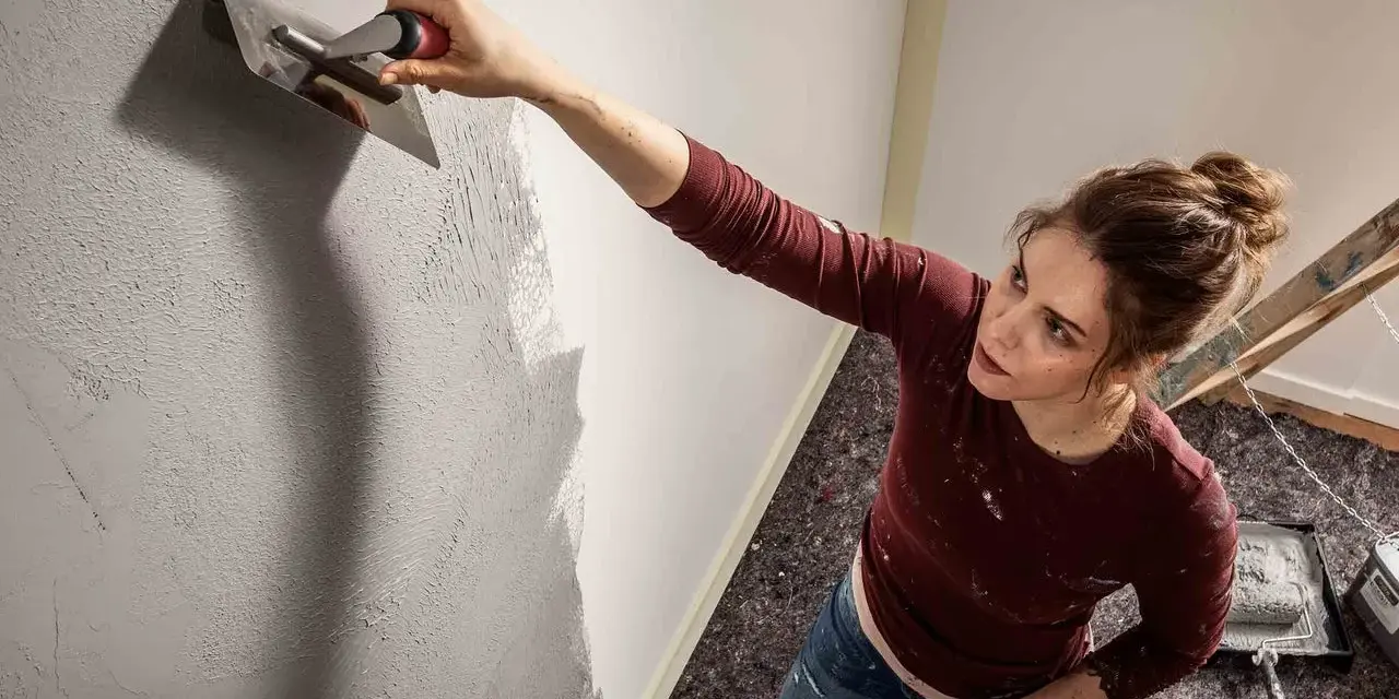 Frau trägt mit einem Spachtel eine Struktur auf die Wand auf. Die Spachteltechnik Wand verleiht dem Raum eine besondere Optik.