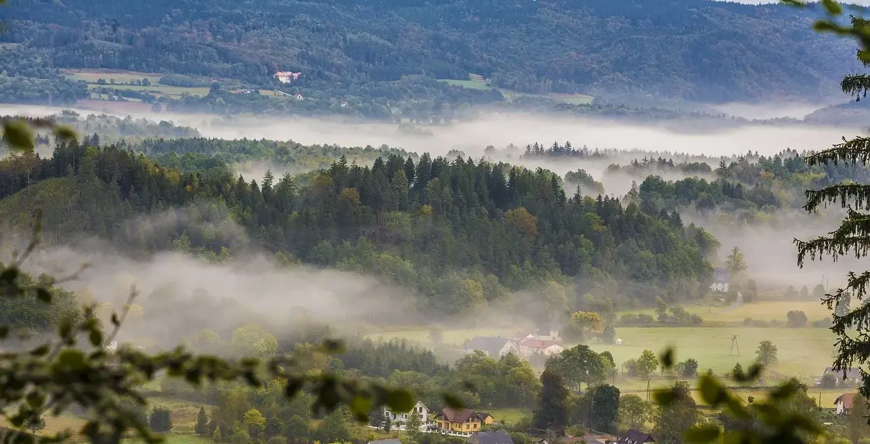 Mgliste poranki nad Sudetami. W oddali widać zamek, a niżej rozciągają się lasy i urokliwe miejscowości.