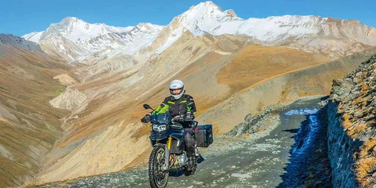 Un motociclista avventuroso affronta un sentiero impervio con la sua jafferau moto, circondato da maestose montagne innevate e paesaggi aridi.