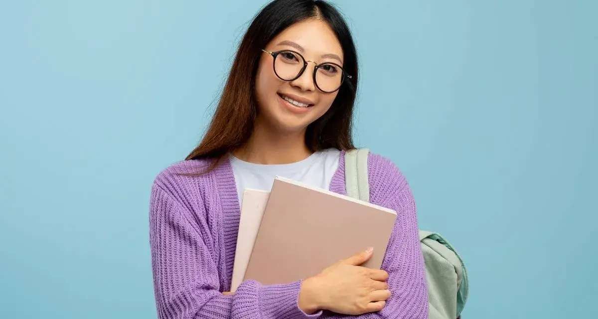 Ragazza con occhiali nuovi per astigmatismo, sorride tenendo libri e zaino.