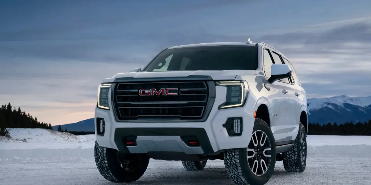 Biały GMC Yukon XL gotowy na zimową przygodę na ośnieżonej drodze, z górami w tle.