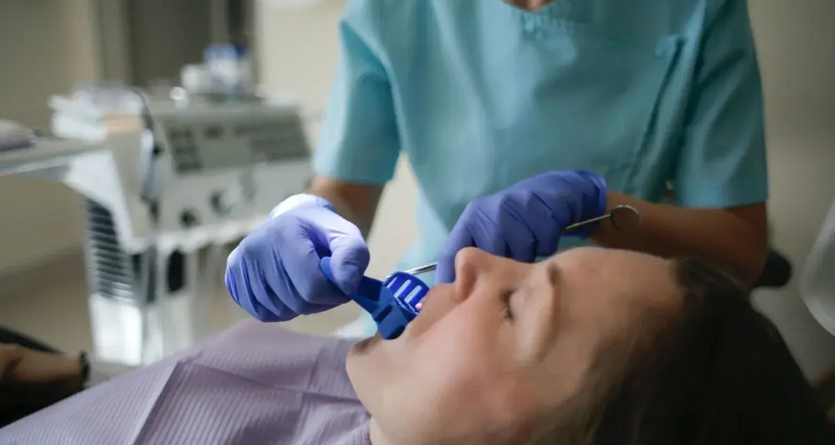 Dentysta w rękawiczkach zakłada pacjentowi niebieski retraktor jamy ustnej.