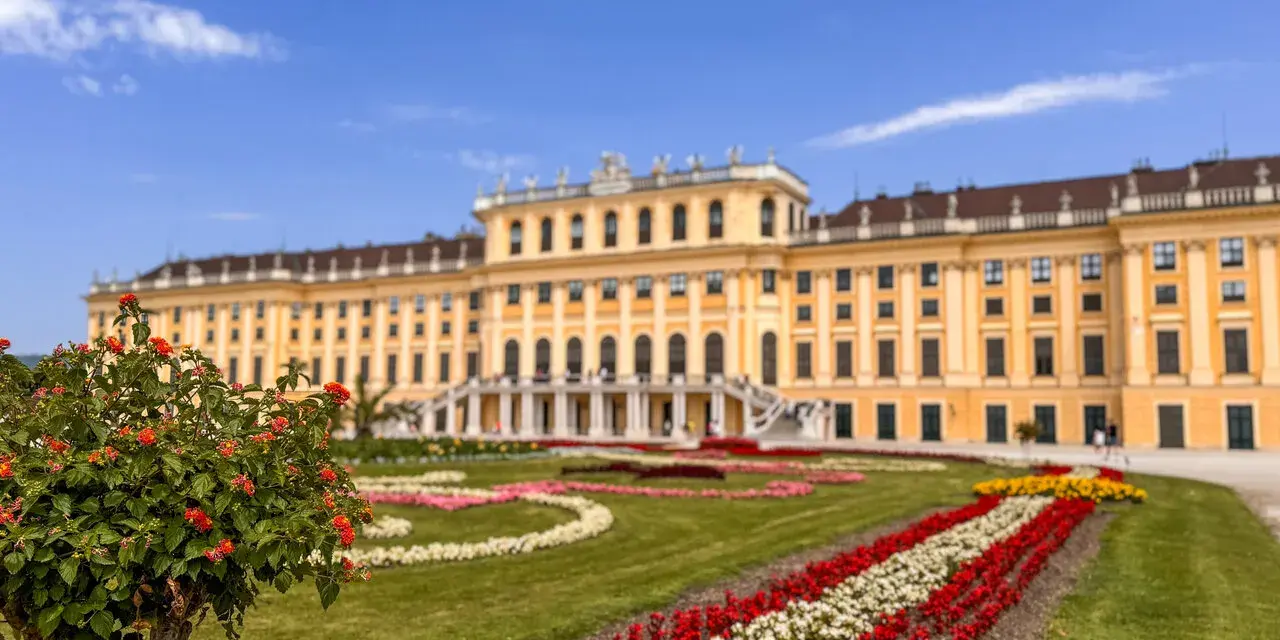 Schönbrunn w Wiedniu, z kwitnącym krzewem w pierwszym planie i barwnymi rabatami kwiatowymi. Idealne miejsce, by zobaczyć w Wiedniu!