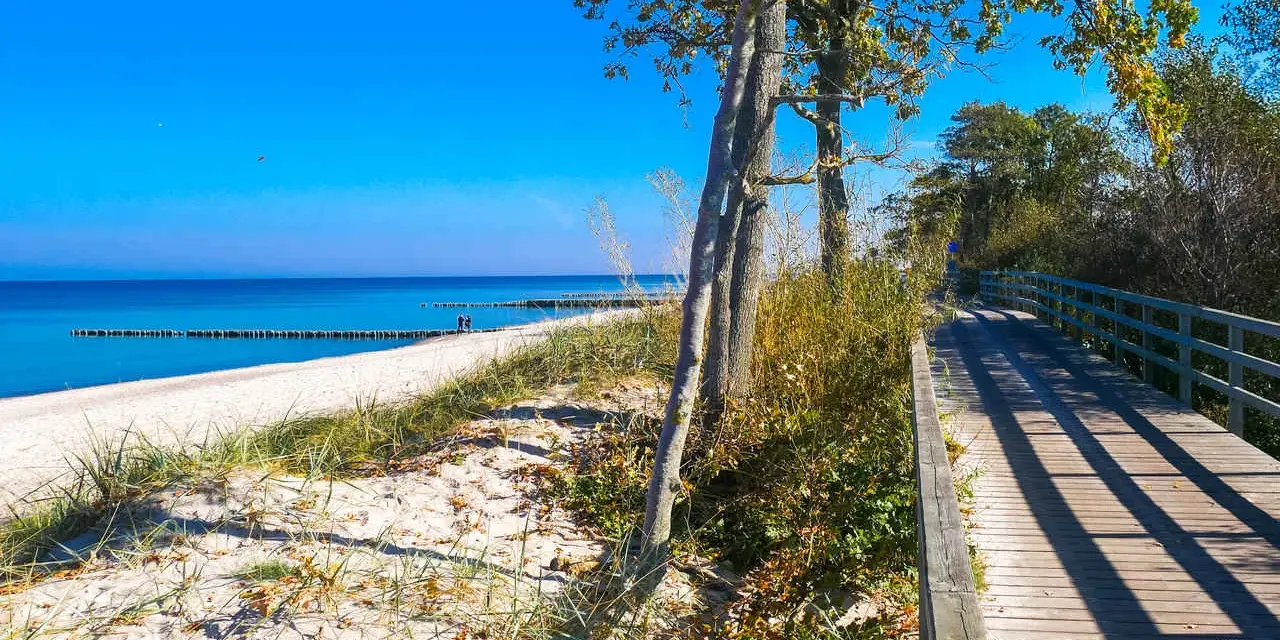 Drewniana kładka prowadząca na piaszczystą plażę nad spokojnym, błękitnym morzem.