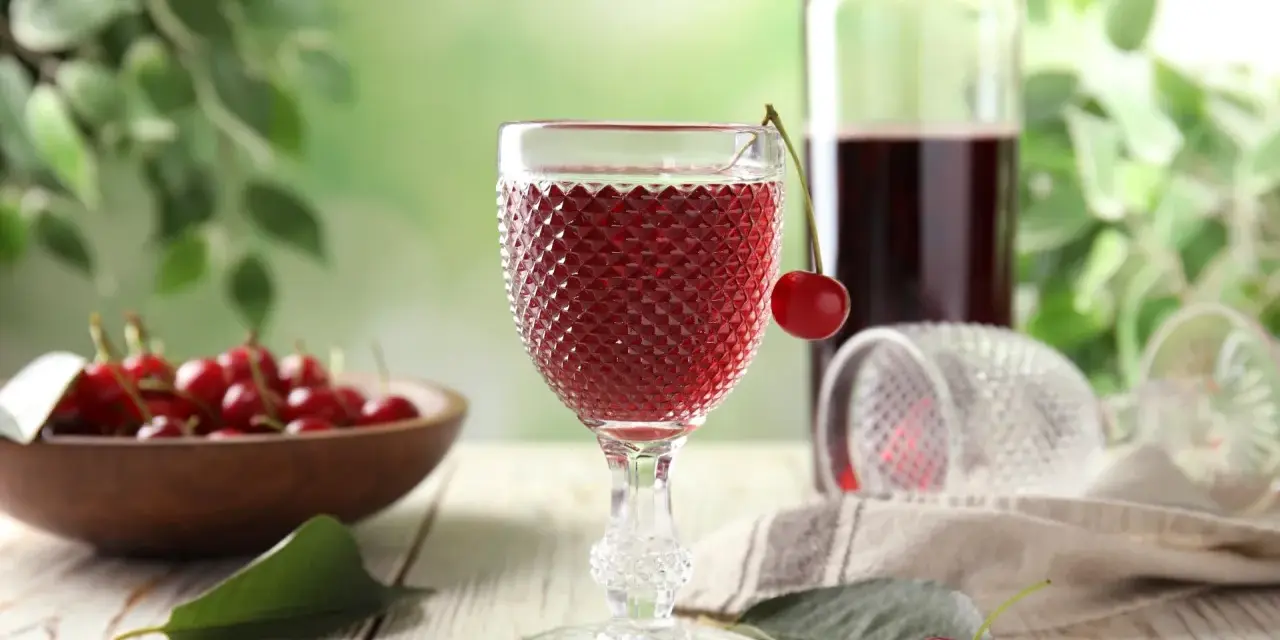 Szklanka z czerwonym winem, wiśnie i butelka. Idealny przepis na wino czerwone z wiśni.
