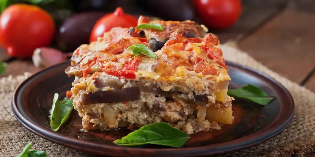 Un assaggio di cosa mangiare a Santorini: una saporita moussaka con melanzane, pomodori e formaggio, guarnita con basilico fresco.