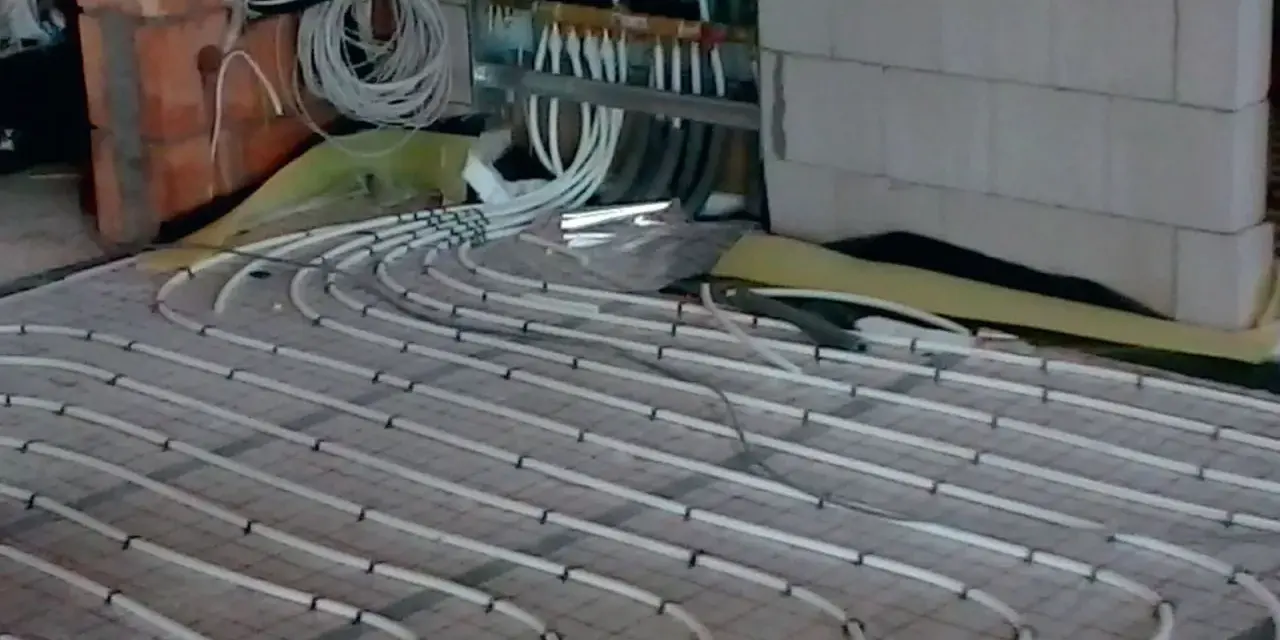 Instalacja ogrzewania podłogowego. Rury ułożone na siatce, podłączone do rozdzielacza. To rozwiązanie obniża koszt ogrzewania.
