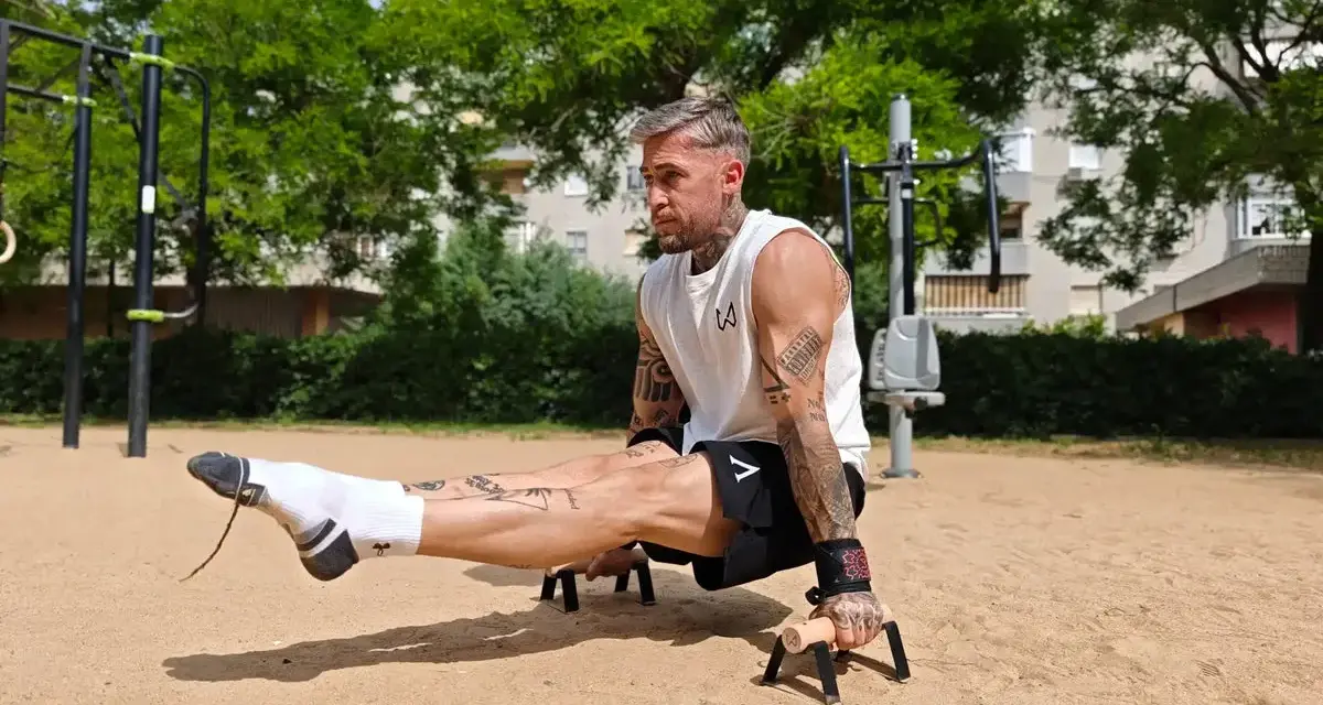 Un homme musclé exécute un exercice de calisthenics, jambes tendues, dans un parc. Un entraînement complet pour un corps athlétique.