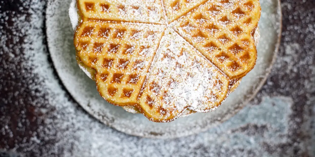 Herzförmige Waffeln, bestäubt mit Puderzucker, auf einem Teller. Ein köstliches Rezept für süße Momente.