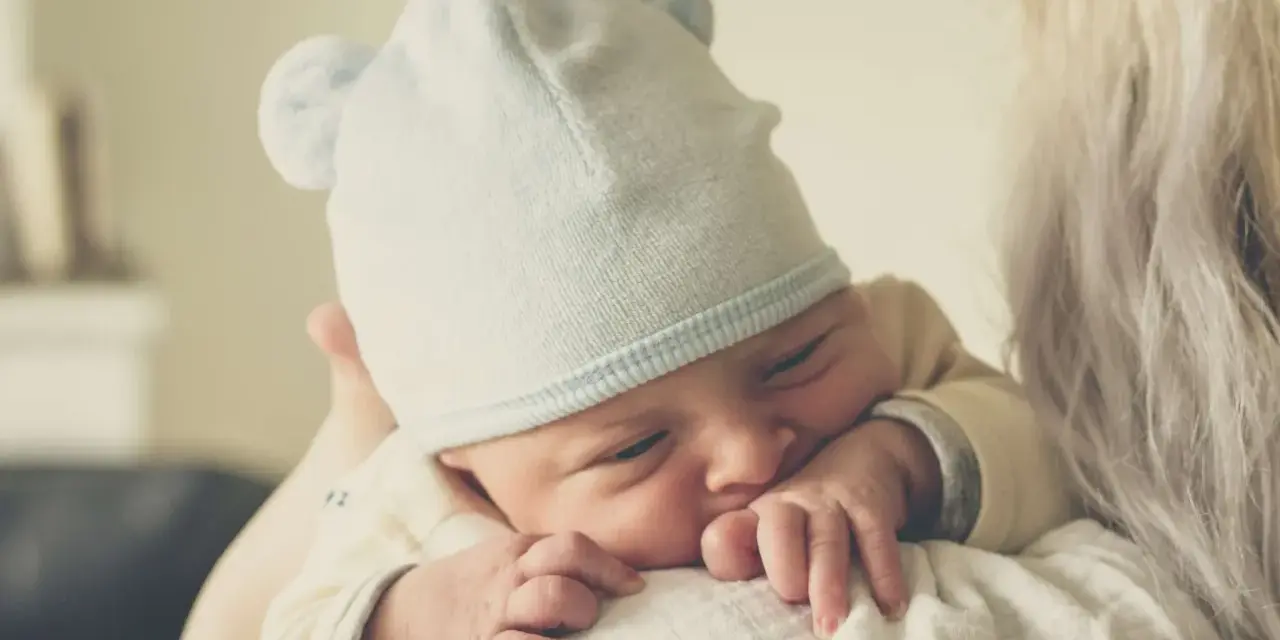 Nyfödd bebis med mössa med öron, tryggt vilande mot en axel. En perfekt baby gåva.