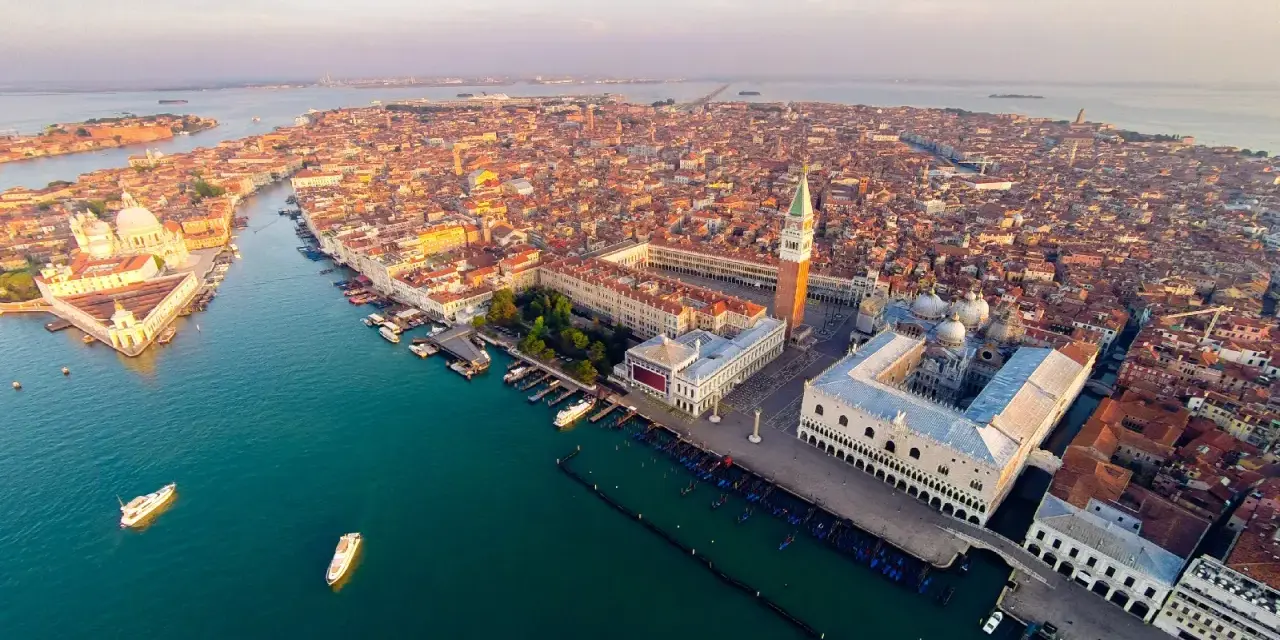 Vista aerea di Venezia al tramonto, con la Basilica di San Marco e il Palazzo Ducale che dominano la scena.