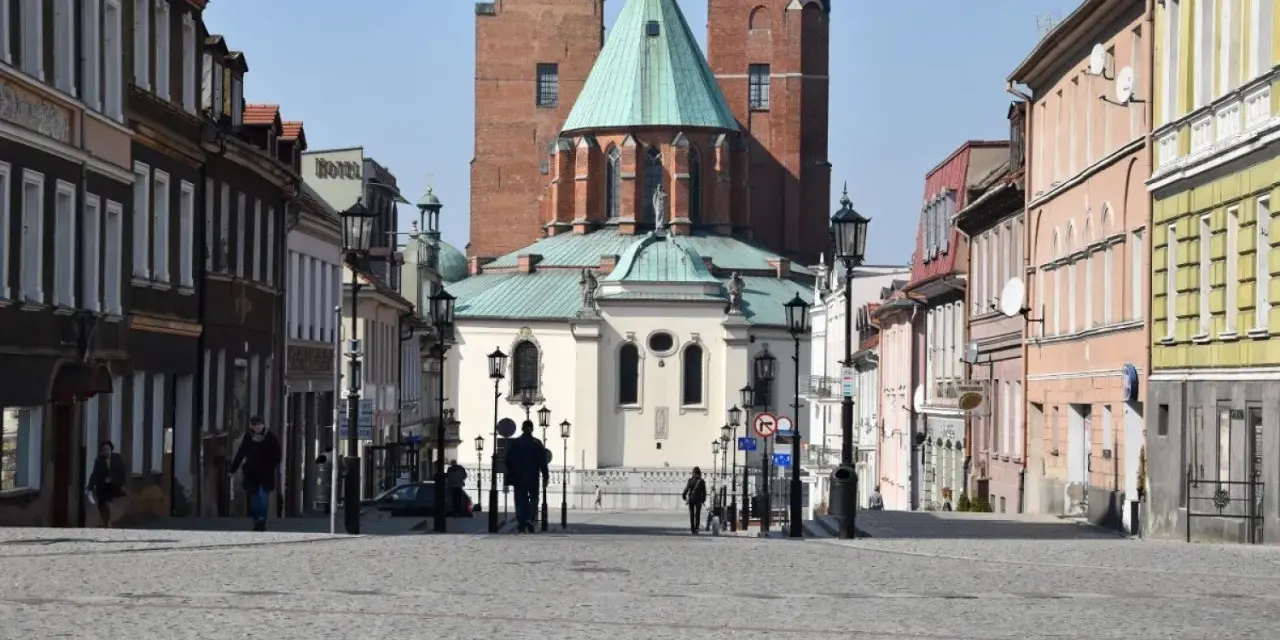 Spacer po brukowanym rynku Gniezna, z katedrą w tle. Kolorowe kamienice po bokach tworzą urokliwą atmosferę.