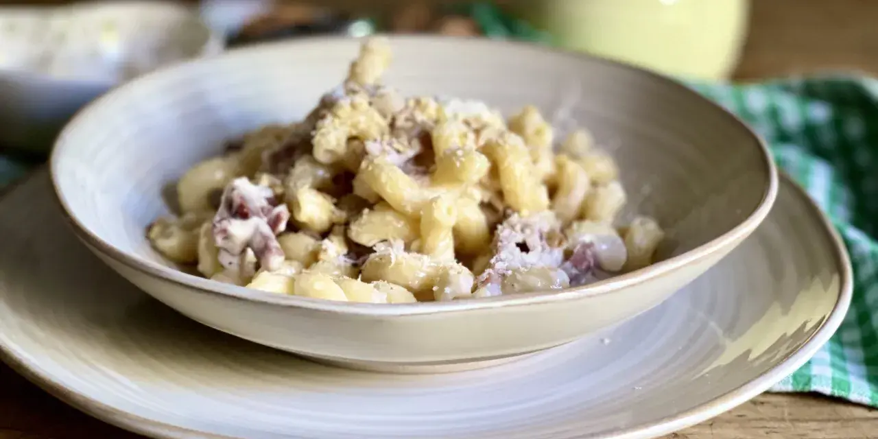 Piatto di pasta con prosciutto crudo, formaggio grattugiato e una salsa cremosa. Un classico confortante.