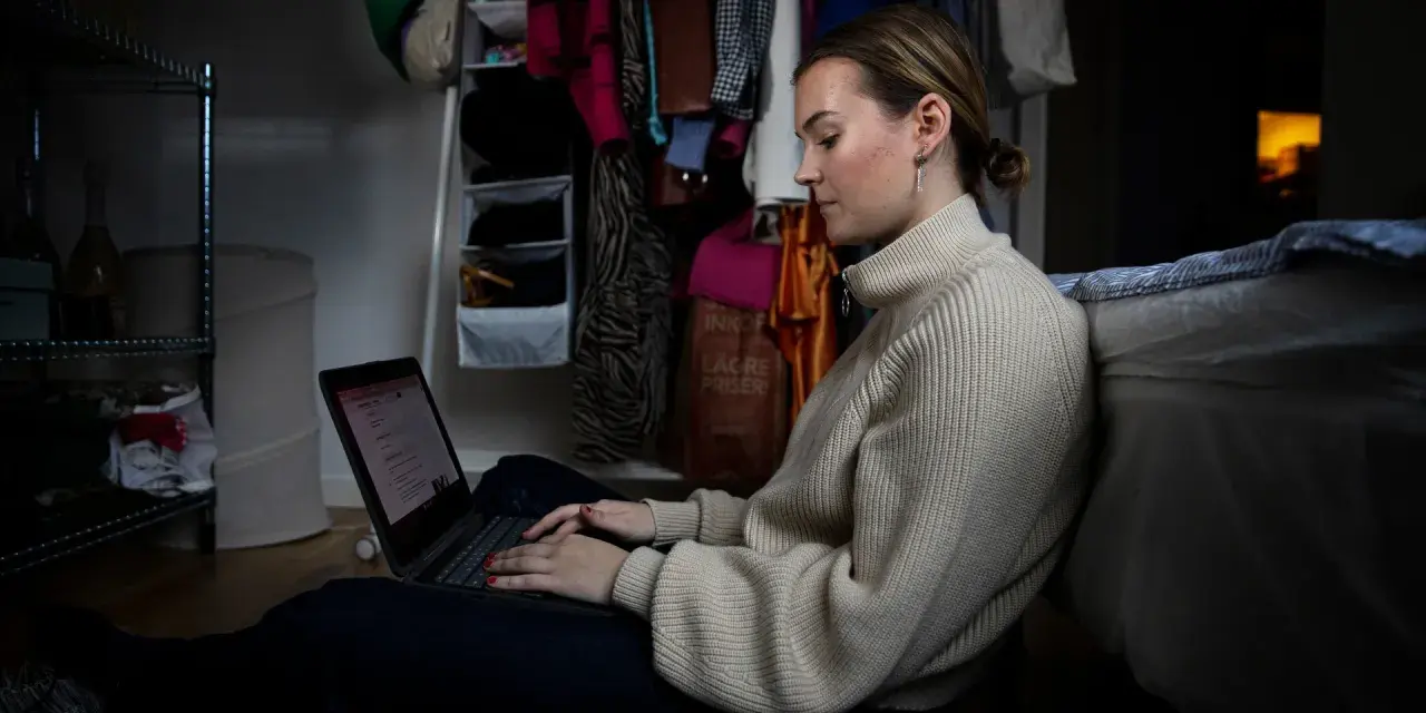 Ung kvinna sitter på golvet och jobbar på sin laptop, hon kombinerar studera på distans och jobba samtidigt.