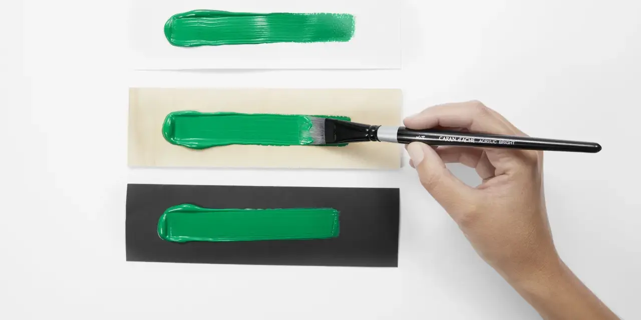 Bandes de peinture acrylique verte sur papier blanc, bois et noir. Une main tient un pinceau, montrant l'application de l'acrylique avant ou après peinture.