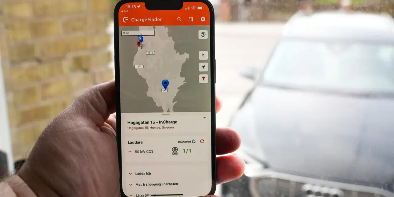 En hand håller upp en mobil med appen ChargeFinder som visar en karta över laddstationer för elbil. En laddapp visar en laddare nära en elbil.