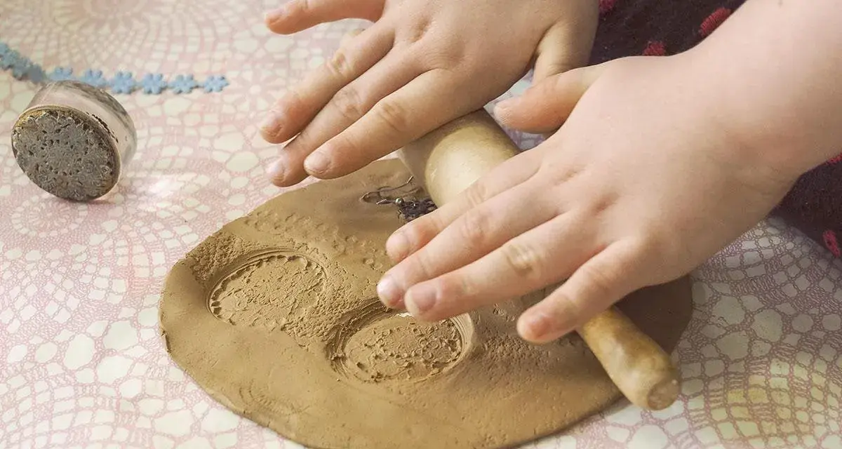 Dziecko wałkiem ugniata glinianą kulę, tworząc wzory. Obok leży stempel.