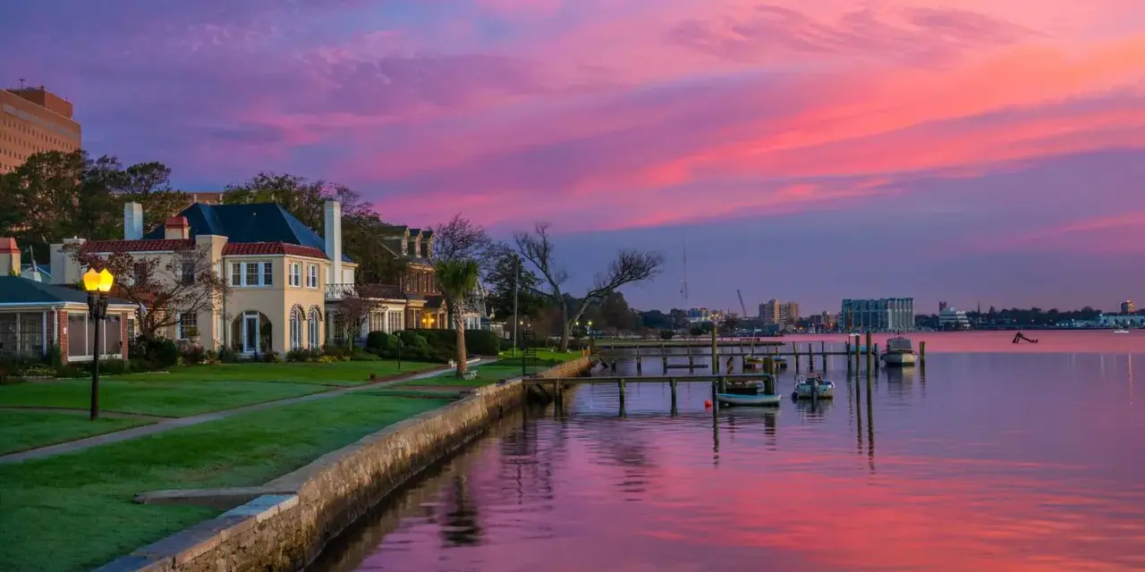Beautiful waterfront homes and boats reflect a vibrant pink and purple sunset, perfect for weekend trips from Richmond, VA.