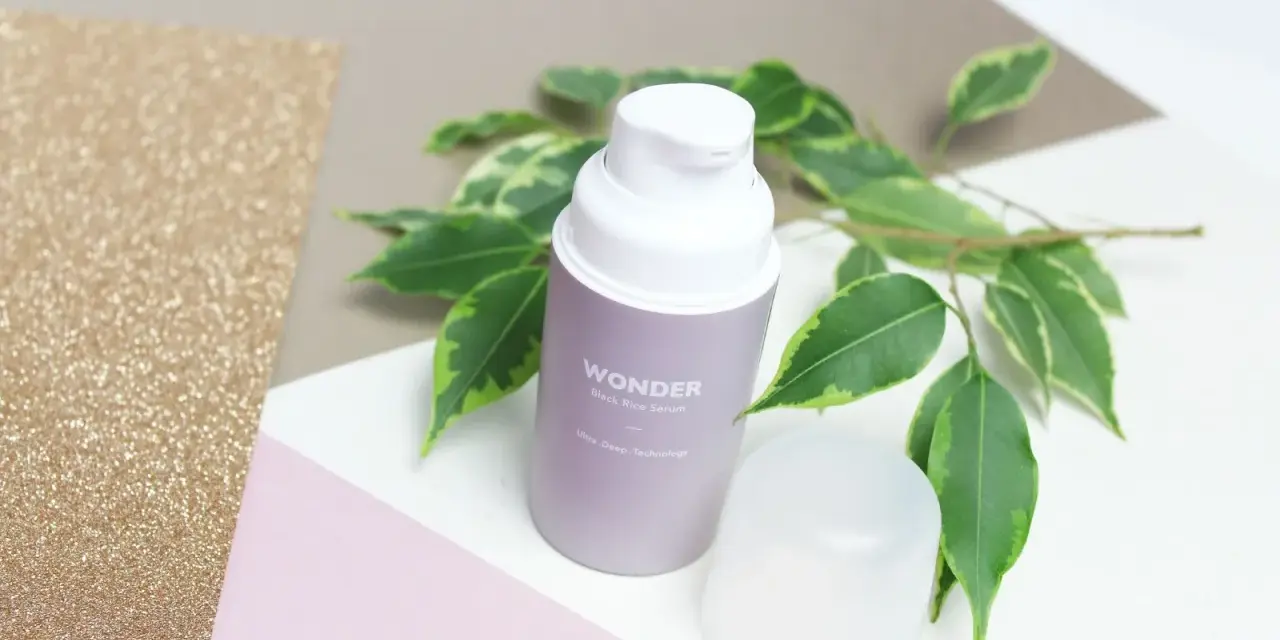 Wondeful! Serum z czarnego ryżu Haru Haru Wonder, otoczone zielonymi liśćmi, na tle błyszczącego złota i pastelowych kolorów.