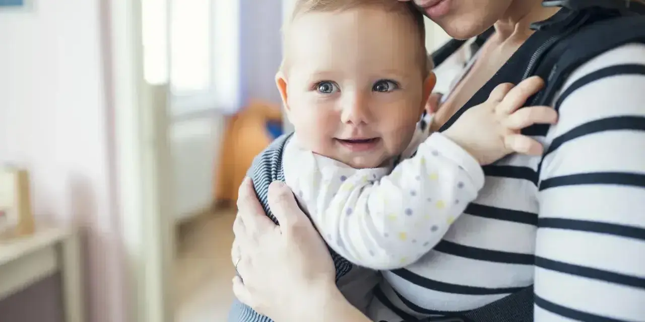 Uśmiechnięte dziecko w nosidle od urodzenia, przytulone do mamy.