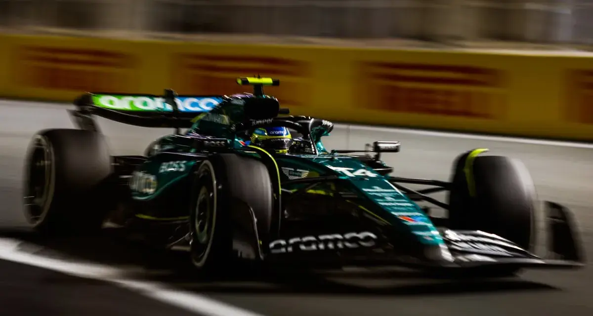 El Aston Martin AMR24 verde y negro acelera en la pista, con el piloto en su casco amarillo.