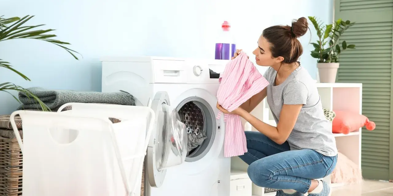 Junge Frau lädt Wäsche in die Waschmaschine. Sie hält ein rosa gestreiftes Kleidungsstück, bereit zum leinen waschen.