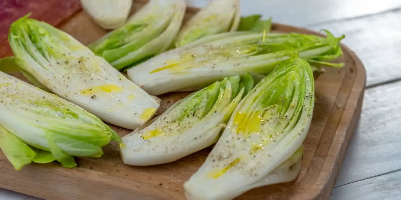 Insalata belga tagliata a metà, condita con olio e pepe, su un tagliere di legno.