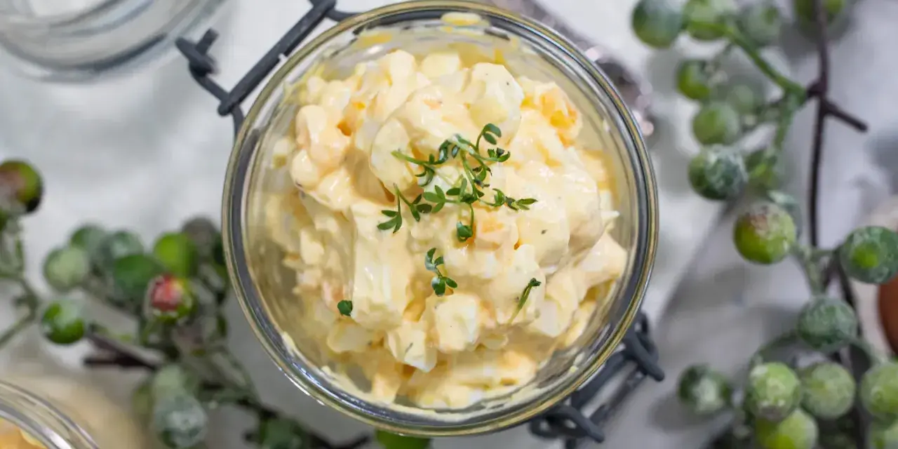 Cremiger Kartoffelsalat mit Fleischsalat, garniert mit frischen Kräutern, in einem Glas serviert.