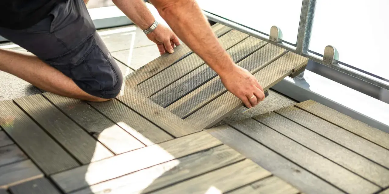 Mann legt Holzfliesen für den dachterrasse gestalten boden. Die Holzoptik passt gut zu modernen Außenbereichen.