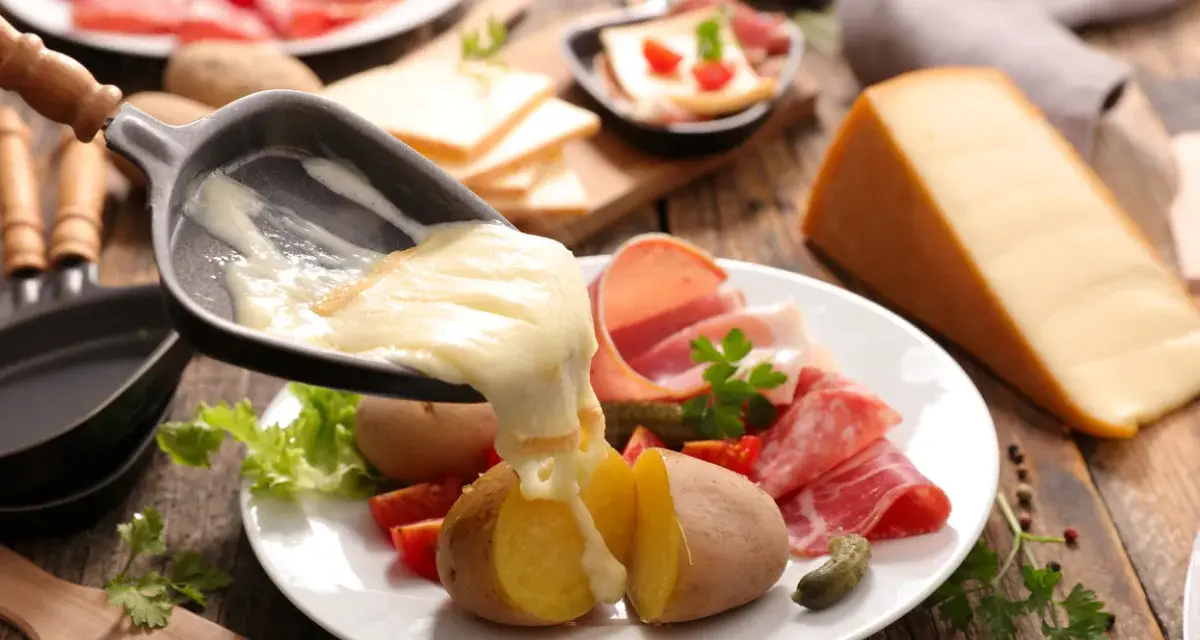 Roztopiony ser z patelni do raclette spływa na ziemniaki i wędliny. Pyszne danie raclette.