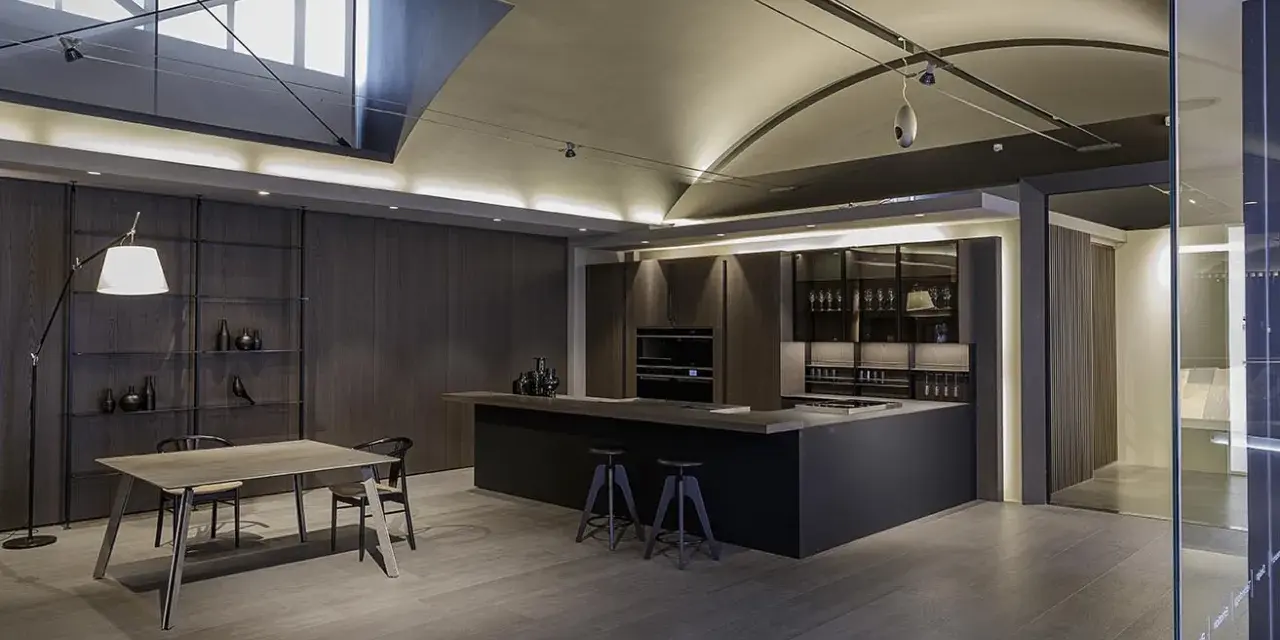 Moderna cocina office con isla central, muebles oscuros, estanterías y mesa de comedor.