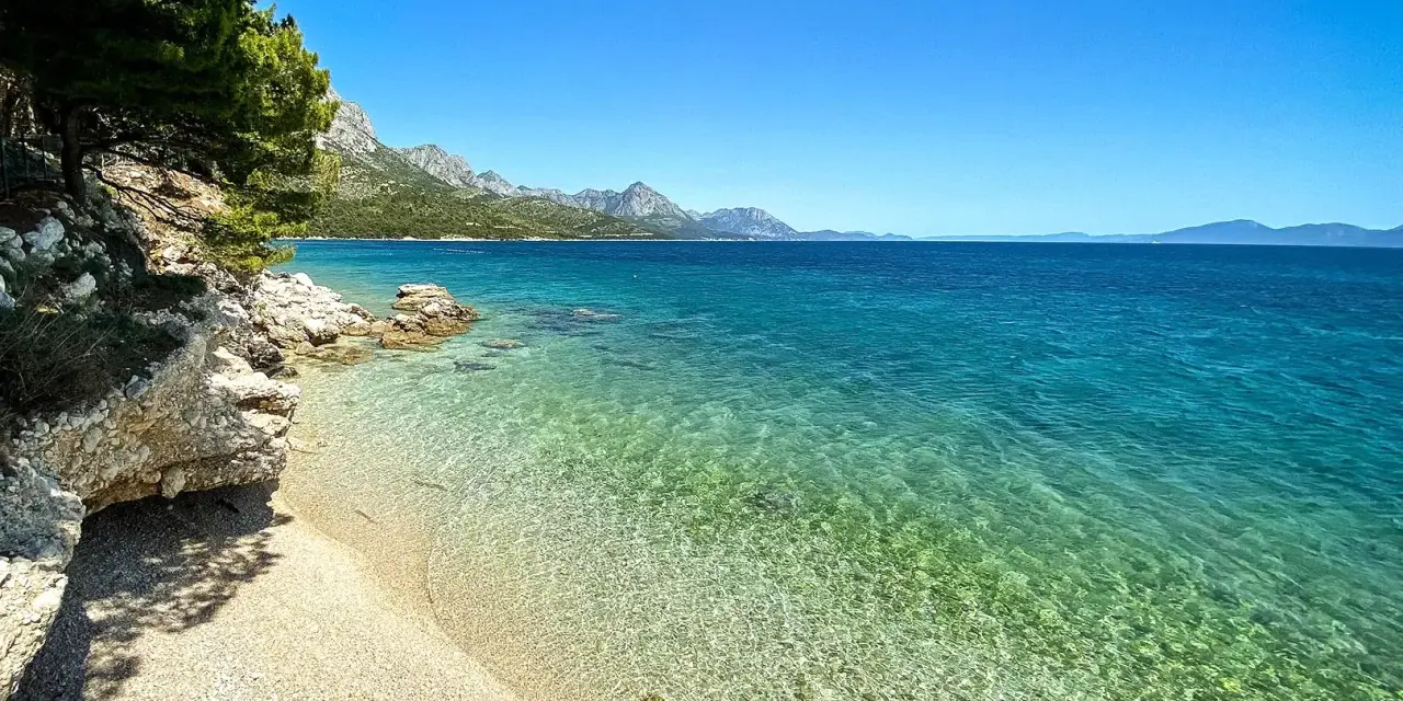Idealne miejsce na camping w Chorwacji: kamienista plaża, turkusowa woda i góry w tle.