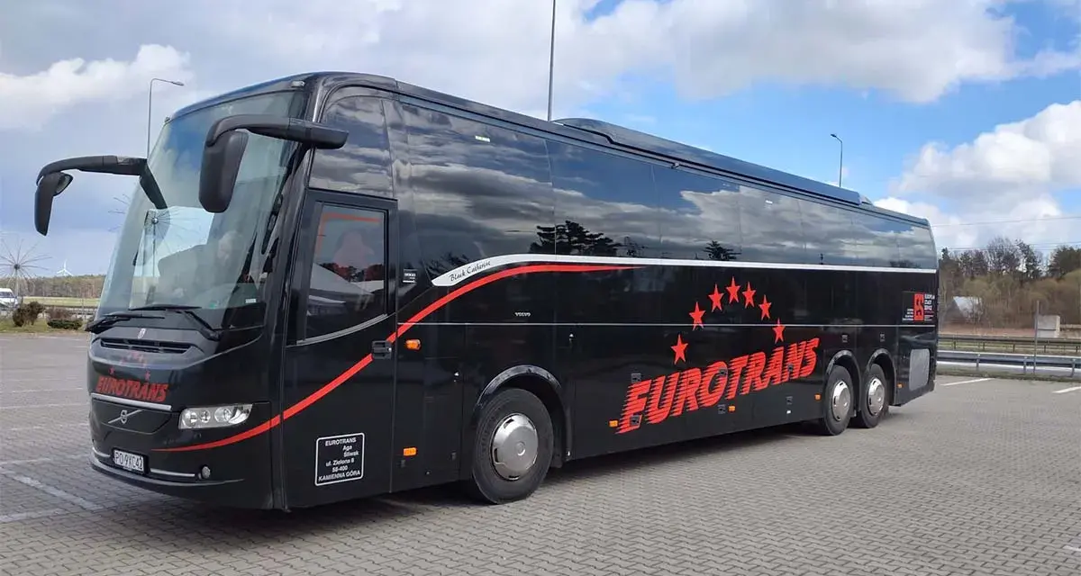Czarny autokar turystyczny Eurotrans z czerwonymi gwiazdami i napisem na tle błękitnego nieba.