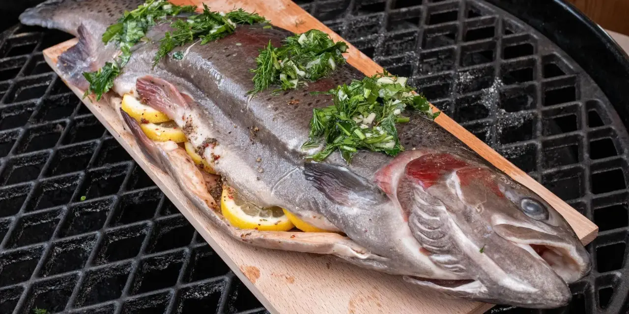 Lachsforelle auf einem Holzbrett, gefüllt mit Zitrone und Kräutern, bereit für den Grill. Die Kerntemperatur ist entscheidend für perfekten Fisch.