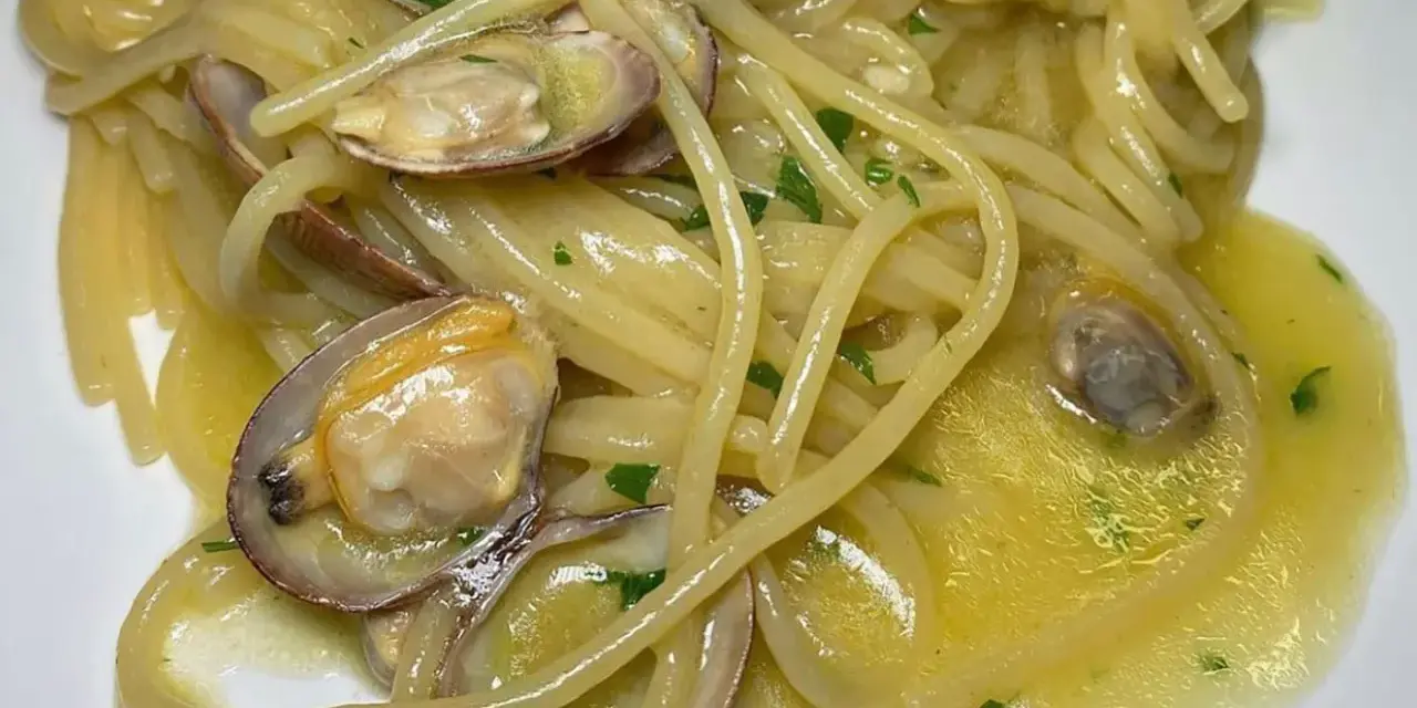 Spaghetti alle vongole cremosi come al ristorante, con vongole fresche e prezzemolo tritato su un letto di pasta dorata.
