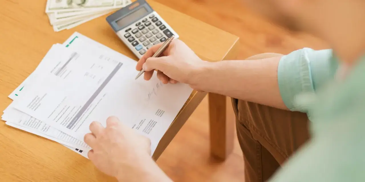 Persona revisa documentos y billetes, calculando cómo hacer un recibo de pago.