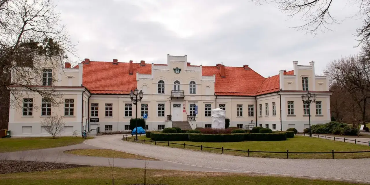Pałac Przebendowskich w Wejherowie, z czerwonym dachem i kremową fasadą, otoczony zielenią i drzewami.