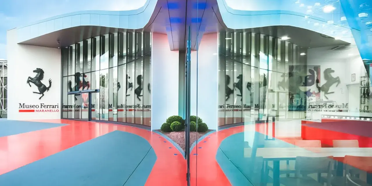 Nowoczesne muzeum Ferrari w Maranello, z charakterystycznym logo i odbijającymi się w szkle sylwetkami koni.