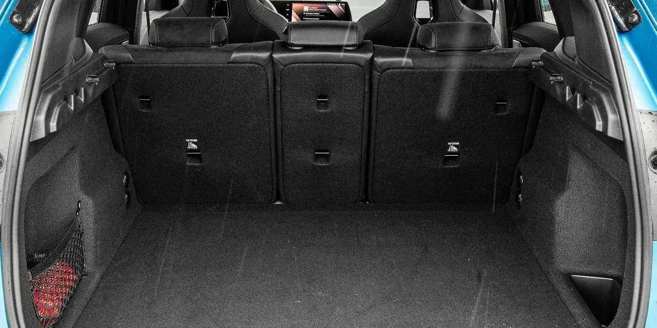 Otwarty bagażnik BMW X1, gotowy na podróż. Widoczne sportowe fotele i siatka z czerwoną gaśnicą.