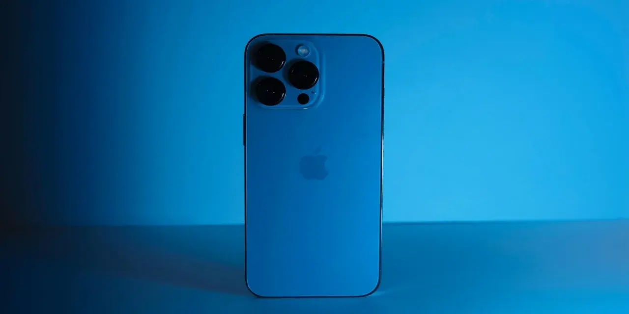 Elegancki iPhone 13 granatowy z potrójnym aparatem, lśniącym na tle niebieskiego światła.