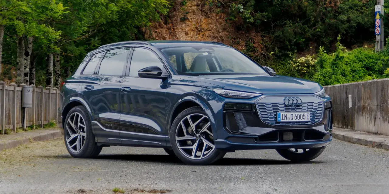 Elegancki, ciemnoniebieski Audi Q6 e-tron stoi na tle zieleni.