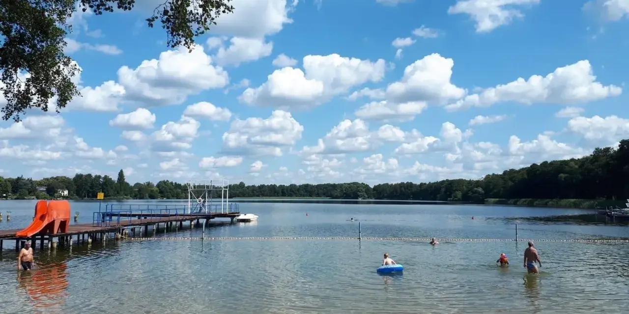 Sommerfreude im Strandbad Heiligensee: Kinder planschen, ein Mann kühlt sich ab, eine Rutsche lockt. Blauer Himmel mit weißen Wolken.