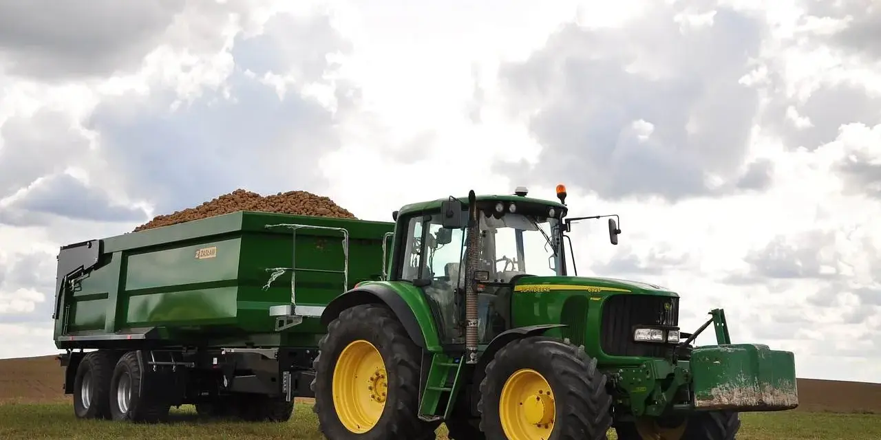 Zielony traktor John Deere z przyczepą wypełnioną ziemniakami na polu.