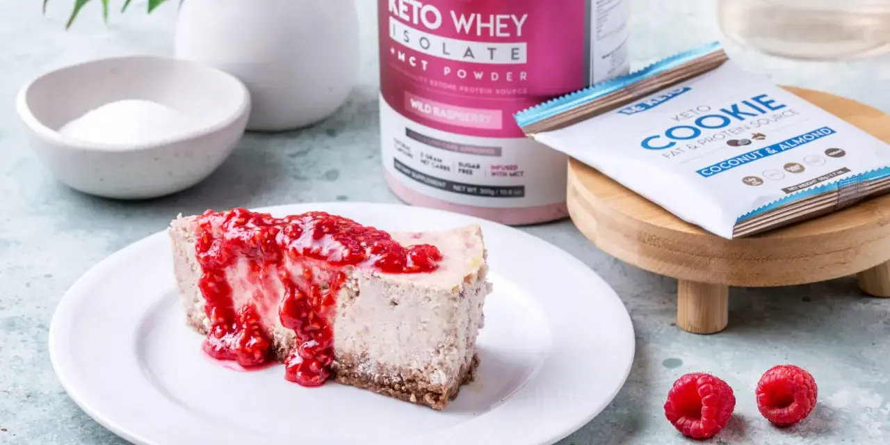 Pyszny sernik keto z malinami, obok słoik Keto Whey Isolate i batonik Keto Cookie. Idealny keto spod do sernika.