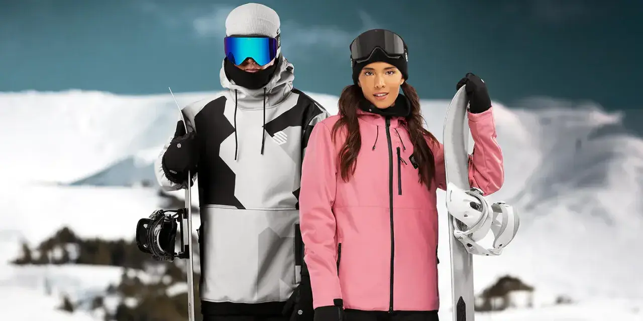 Pareja con tablas de snowboard, ella con chaqueta rosa, él con chaqueta gris y negra. Opiniones sobre Sorona Aura: ¡calidez y estilo en la montaña!